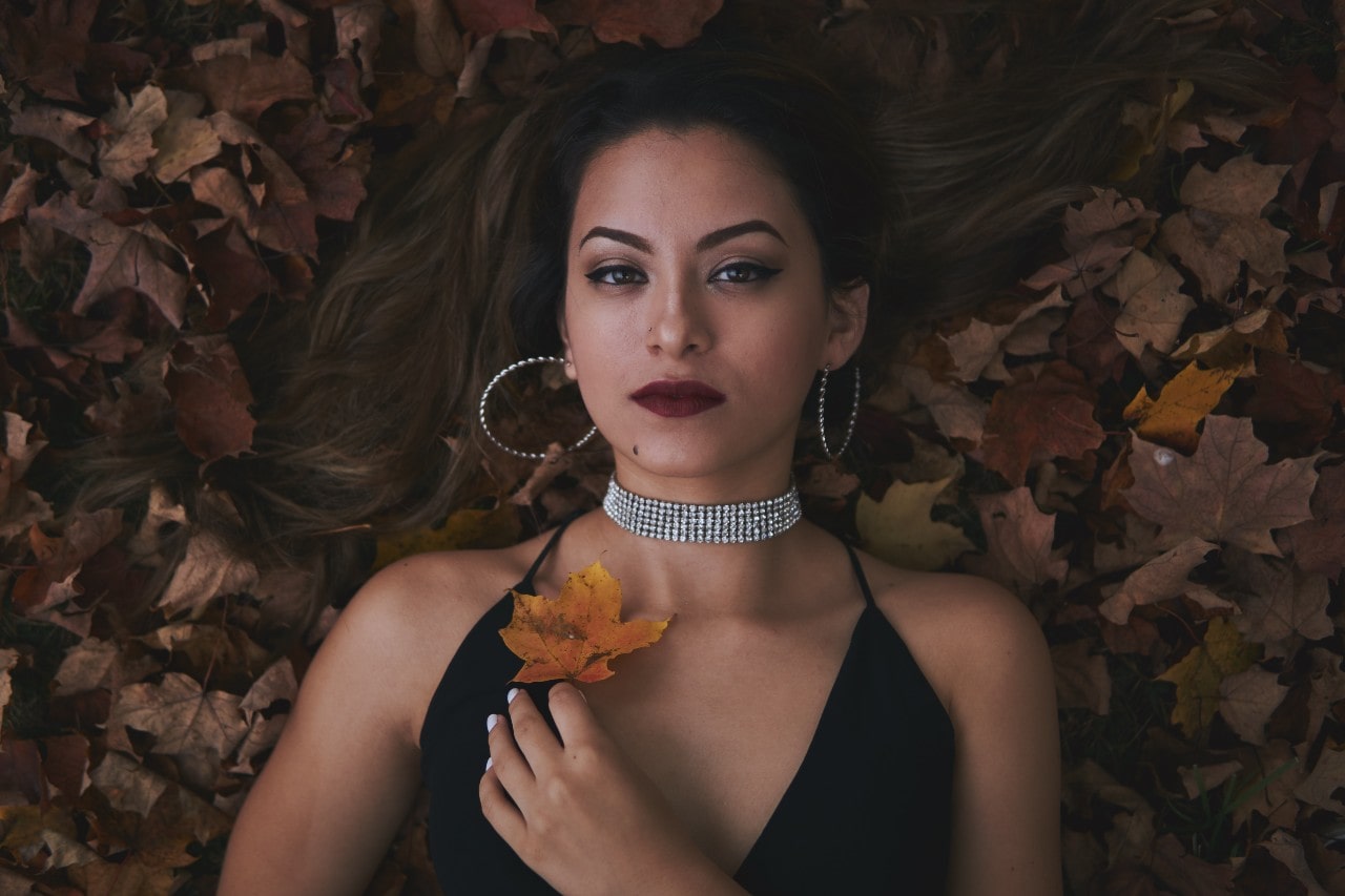 a woman laying in fall leaves, wearing a pair of diamond hoop earrings and a diamond choker