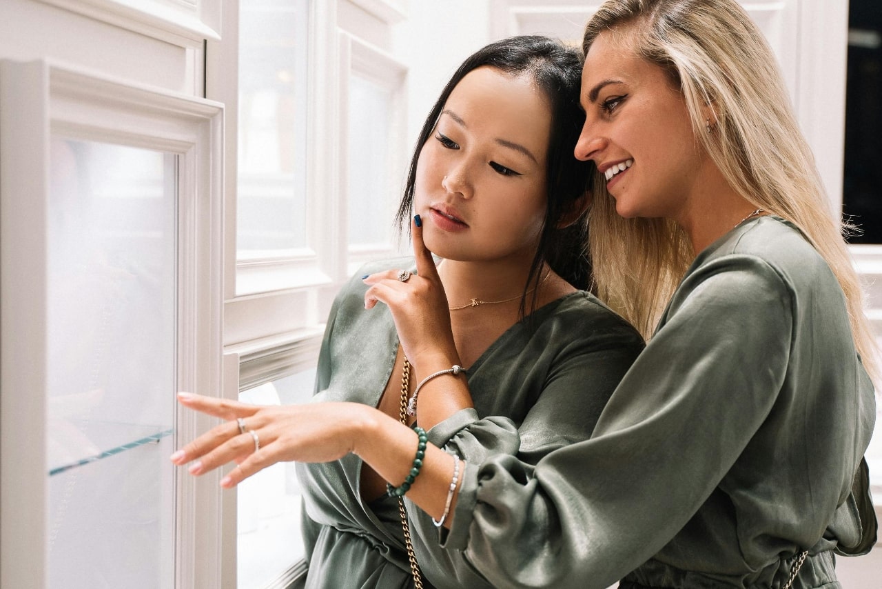 Two woman in a green sating blouses glance at the jewelry counter