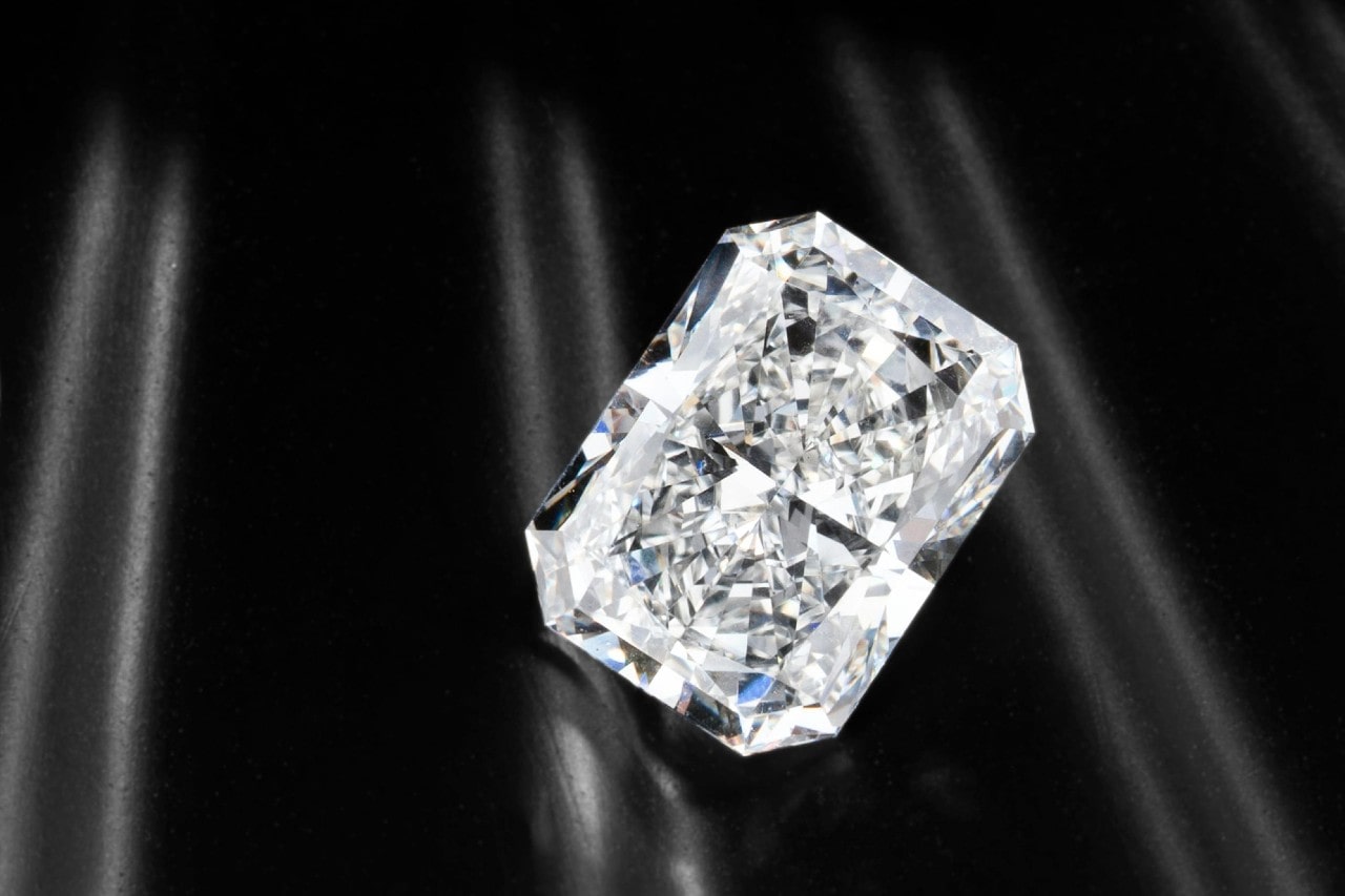 A sparkling, emerald-cut diamond rests on a sleek black surface.