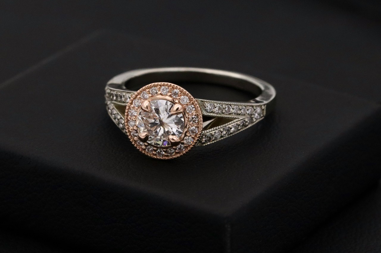 A white gold and rose gold halo engagement ring with diamonds along the split band