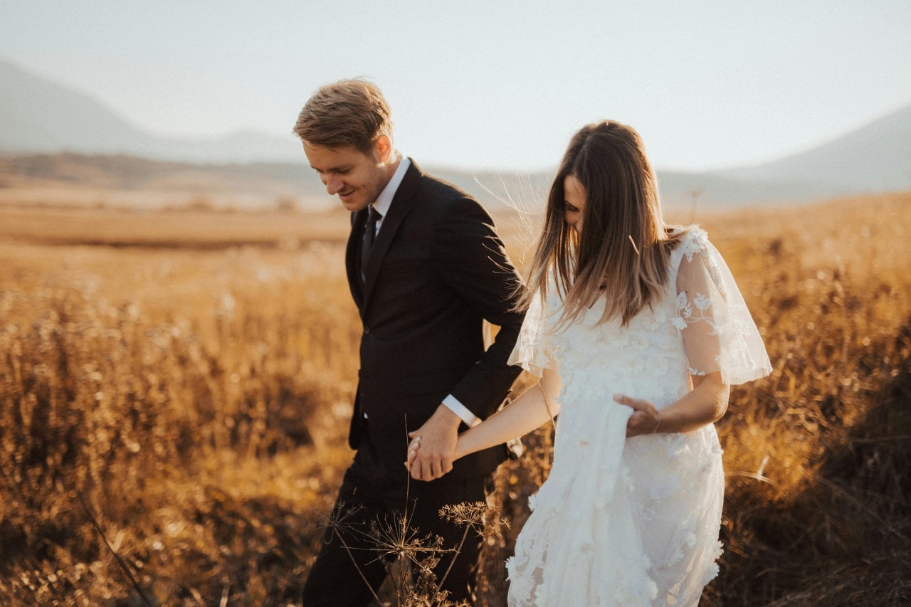 a bride and groom holding hands in a field