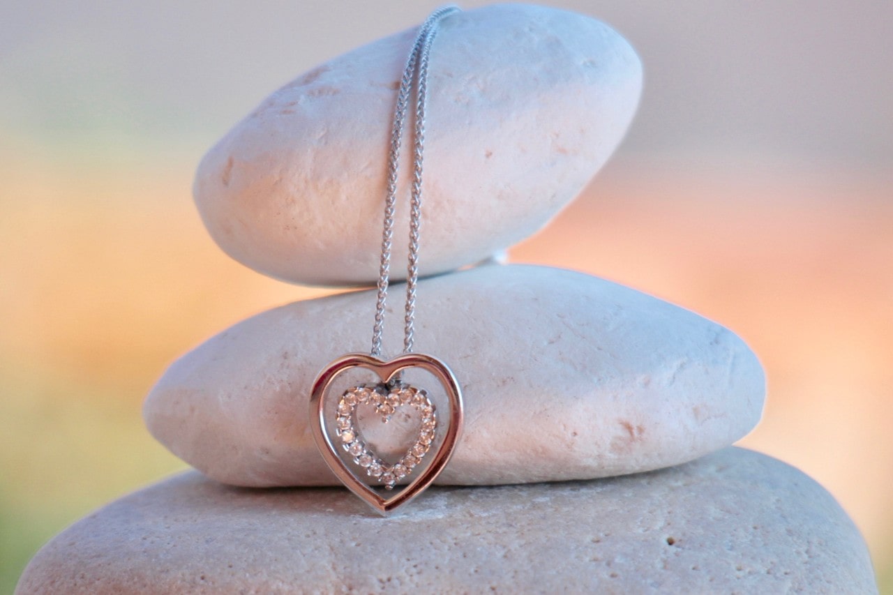 three stones stacked on top of each other with a heart-shaped pendant necklace draped over them