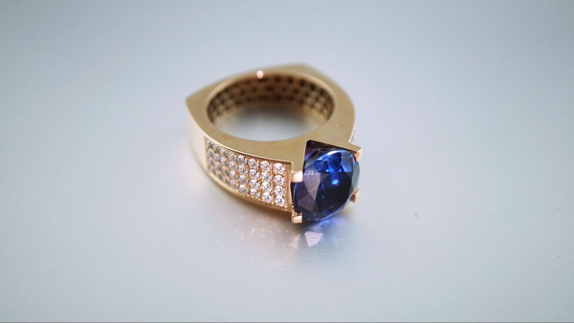 a yellow gold ring featuring a sapphire center stone and diamond accent stones on a gray surface