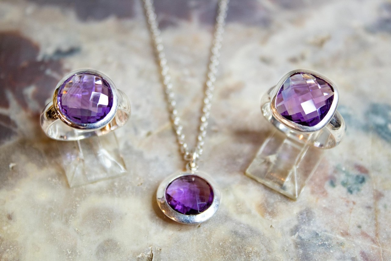 a set of amethyst jewelry in bezel settings on a textured surface