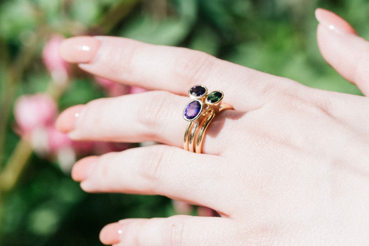 close up image of a woman’s hand wearing a stack of gemstone fashion rings