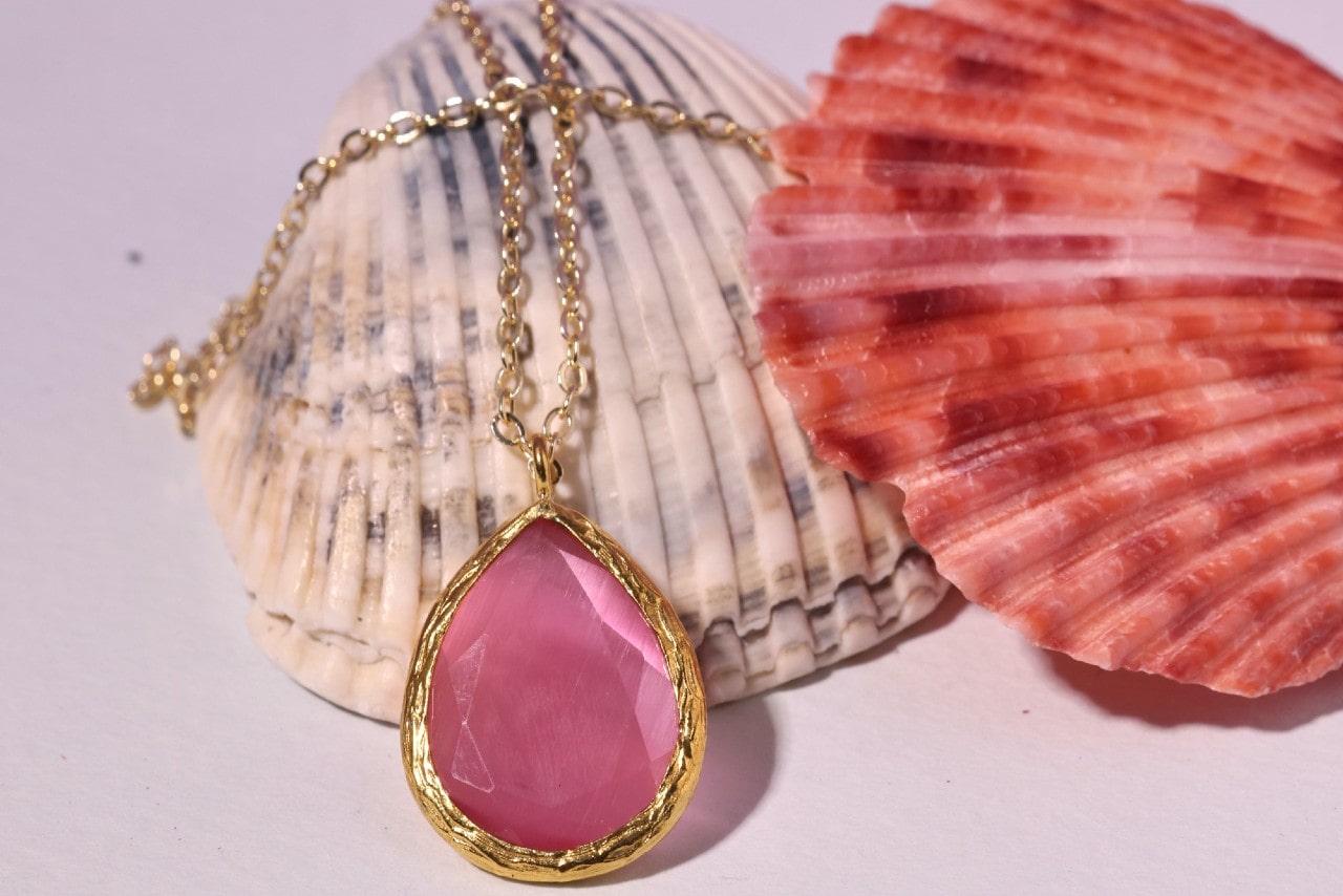 a yellow gold necklace with a pink gemstone pendant lying on two sea shells