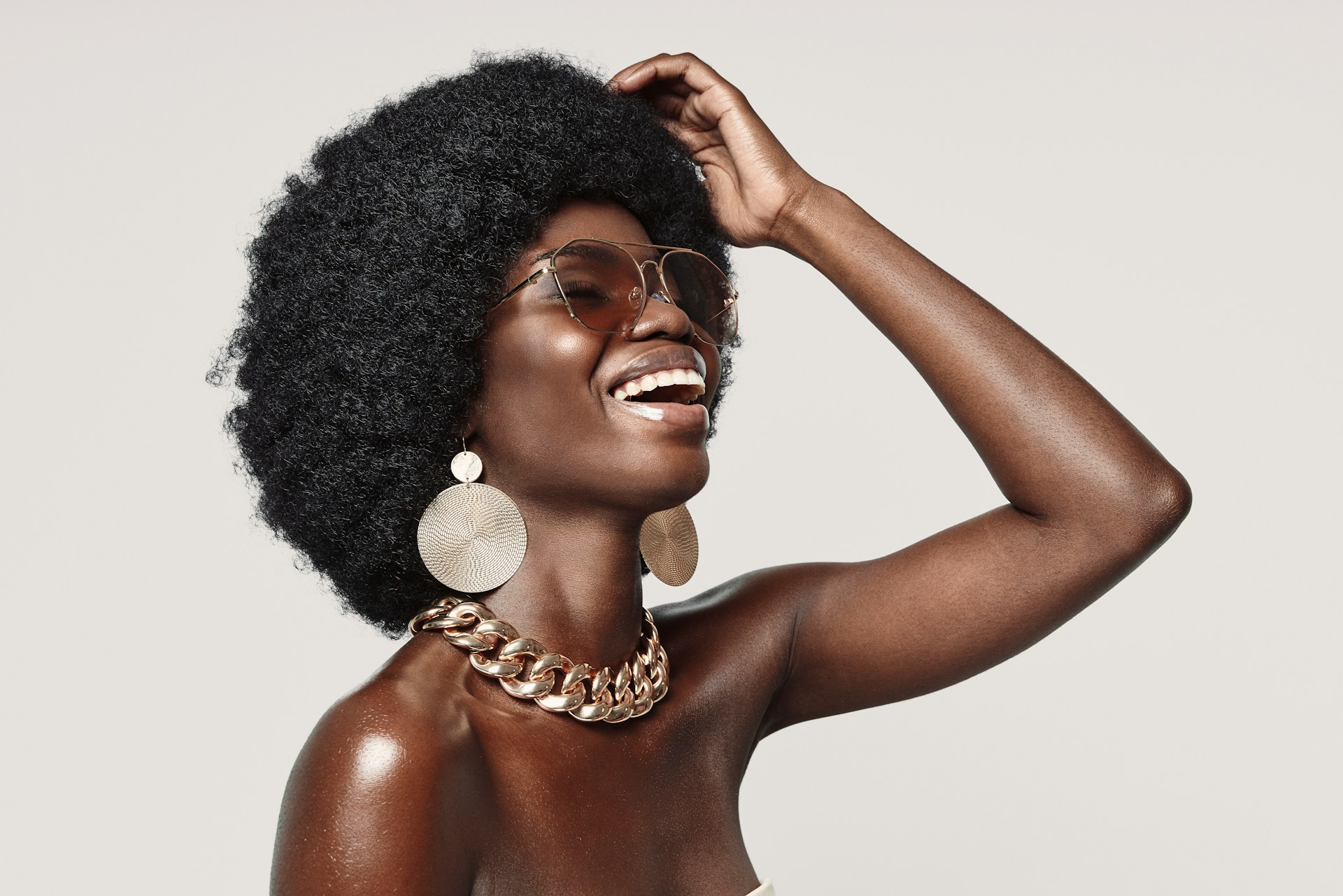 A view of a woman in a chunky chain necklace, large earrings, and sunglasses.