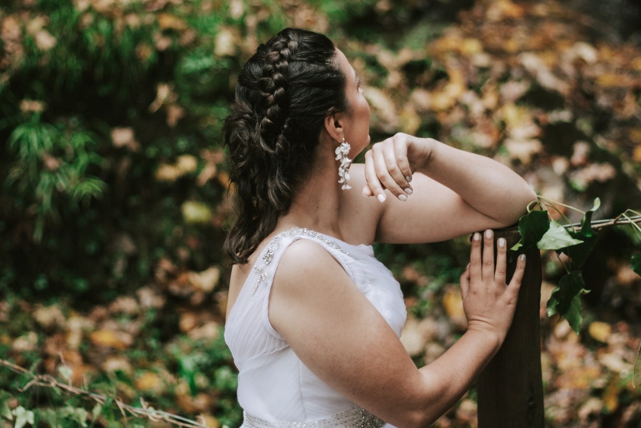 A bride in sleeveless, open back dress looking at the autumn scenery ahead of her.