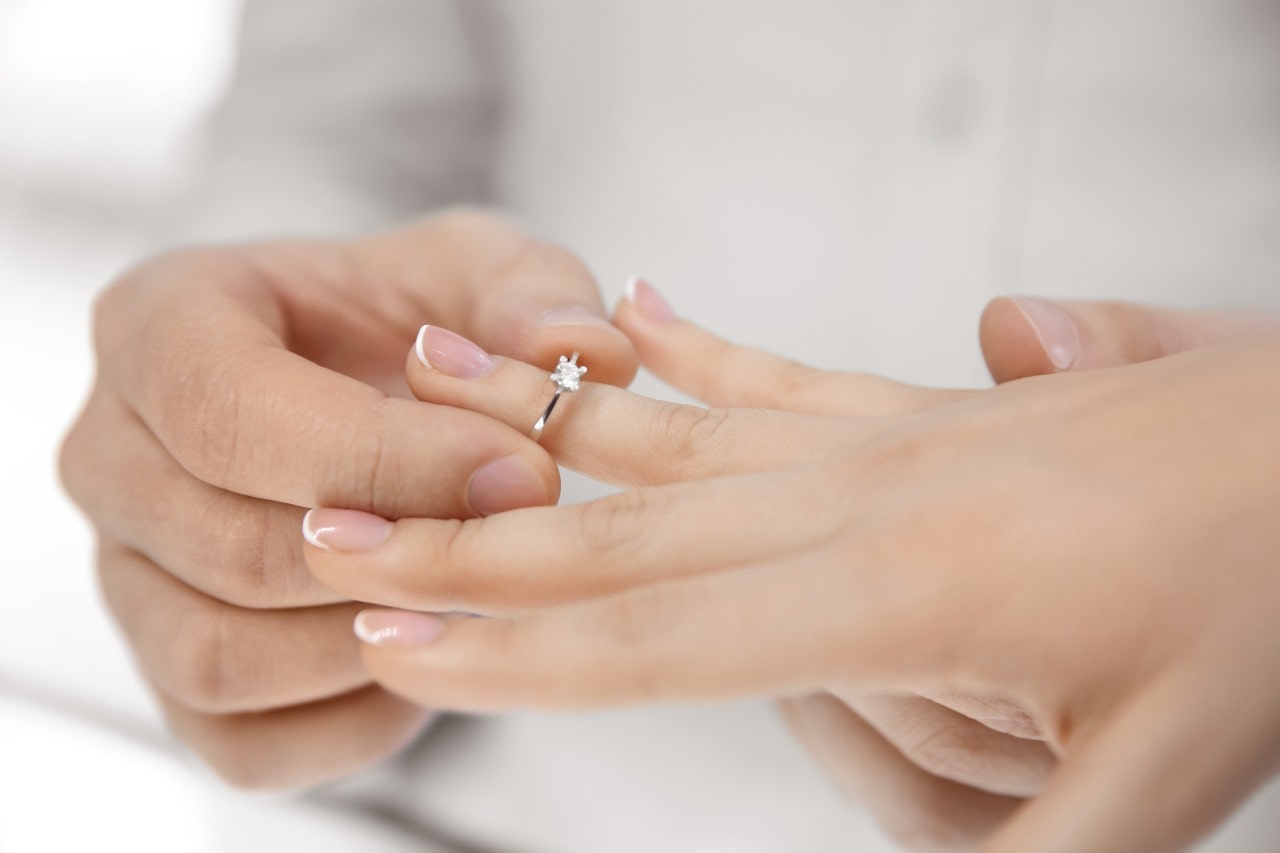 Close-up of a person placing an solitaire diamond engagement ring on another's finger