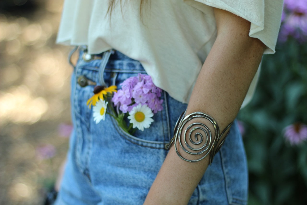 A closeup of a woman wearing a swirling silver bangle outside.