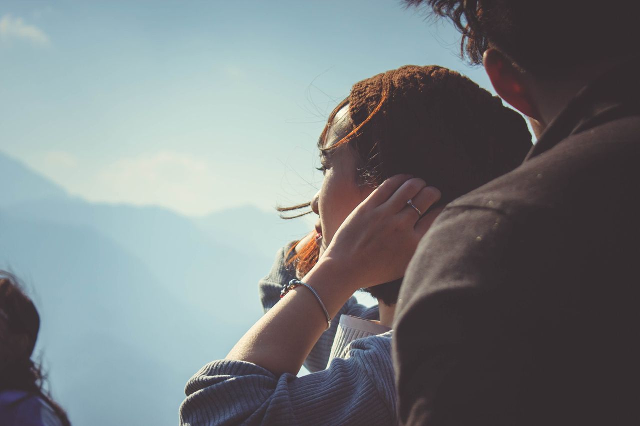 A woman wearing a silver bracelet tucks her hair behind her ear while enjoying a view.