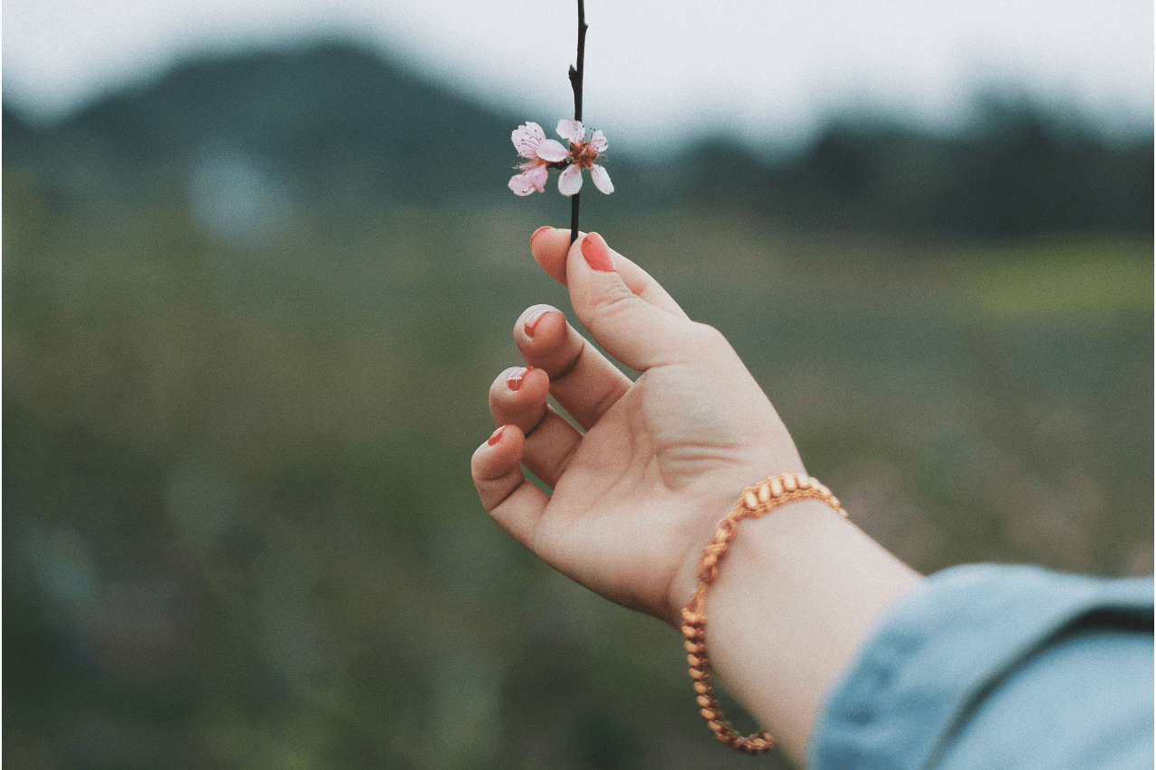 A woman holding a blossom wears a rose gold chain bracelet.