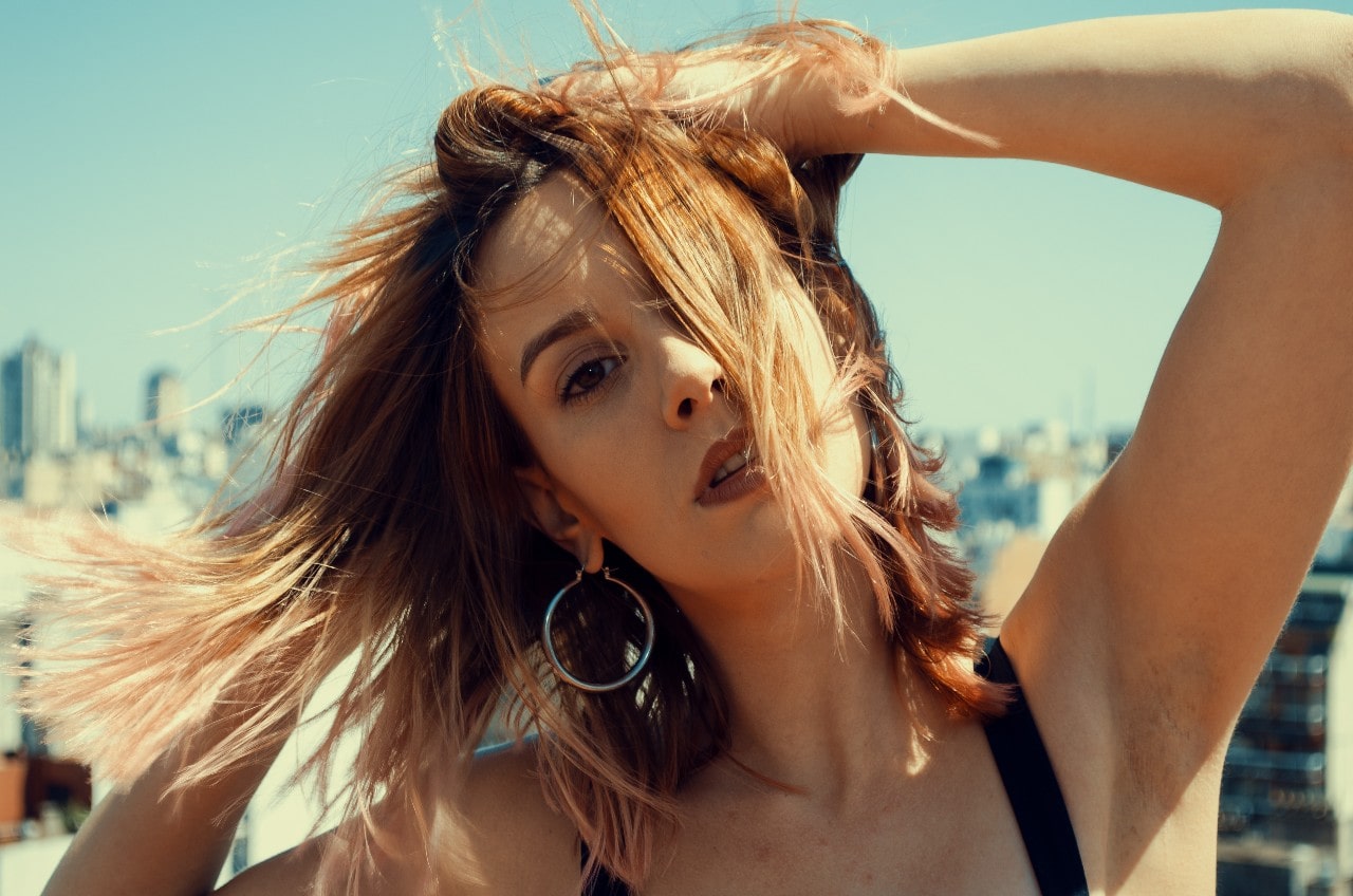 A woman standing on a roof, posing as the wind blows with white gold hoop earrings.