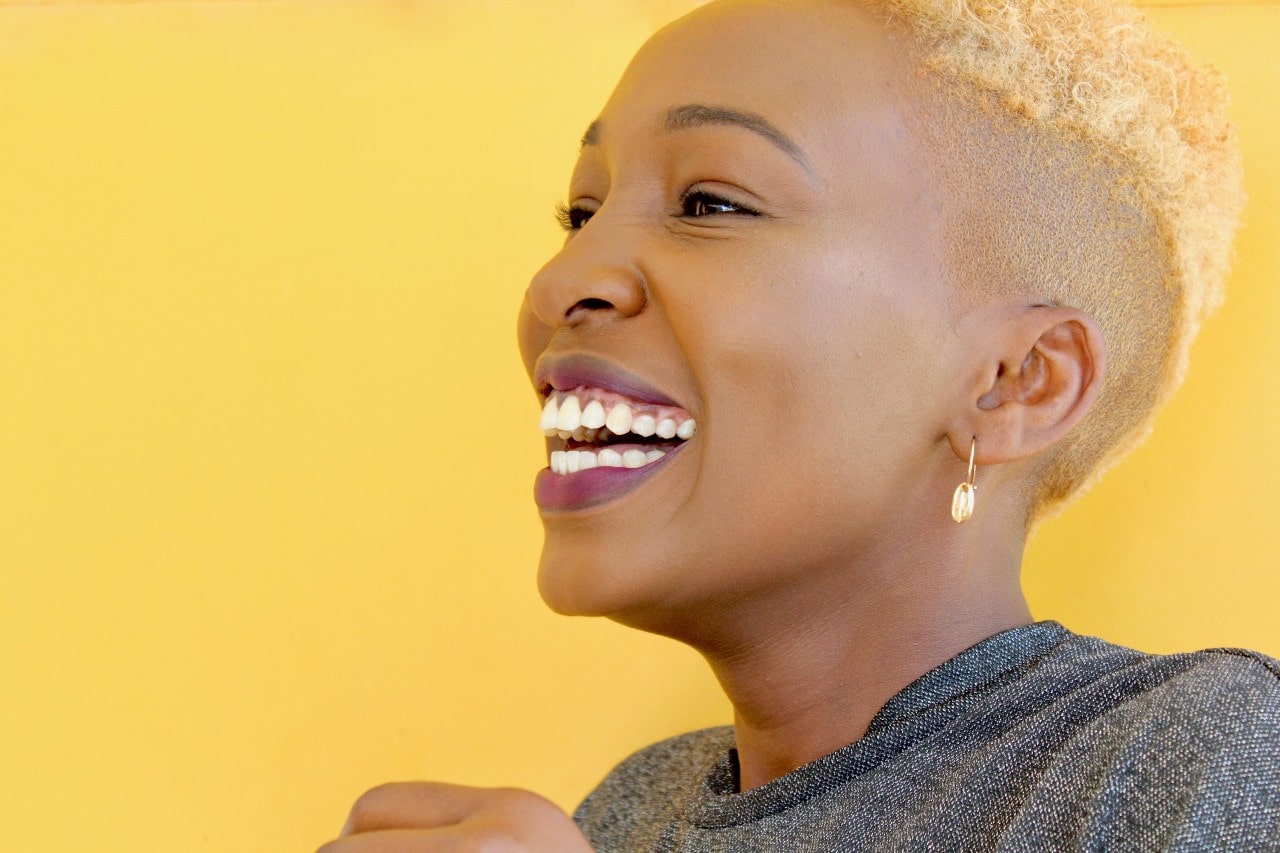 A woman in a studio laughs while wearing gold diamond drop earrings.