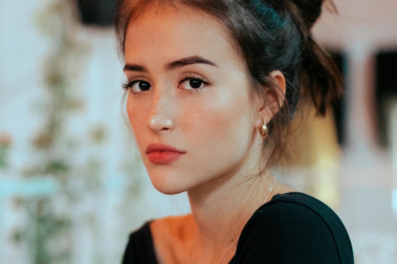 A woman in a black top wears gold huggies earrings.