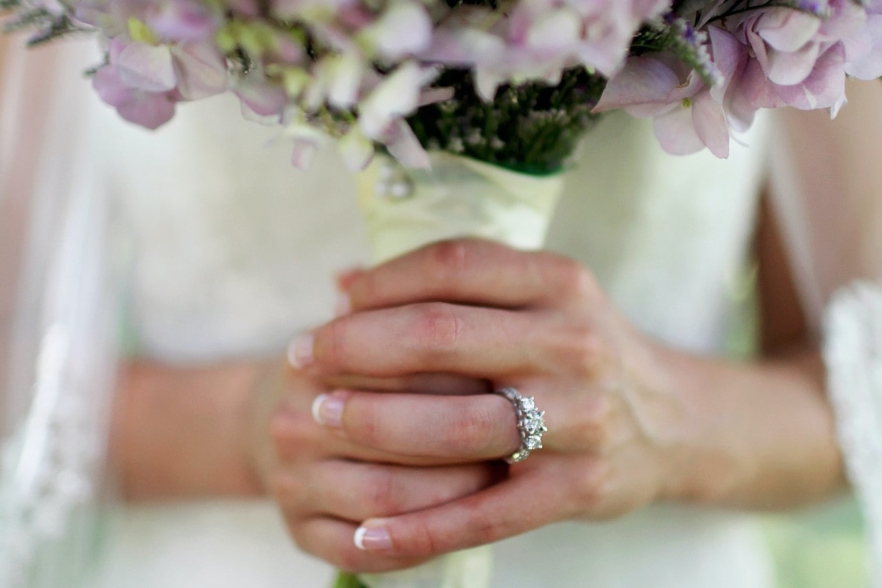 a bride holding a bouquet of flowers and wearing a three stone engagement ring