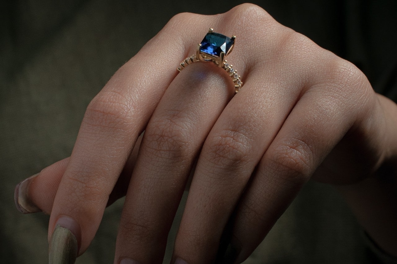 a lady’s hand wearing a beautiful fashion ring with diamonds and a blue gemstone
