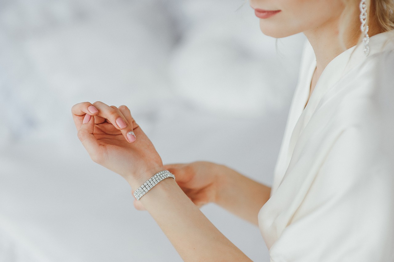 A woman in a white blouse fixes her diamond tennis bracelet. A woman in a white blouse fixes her diamond tennis bracelet.