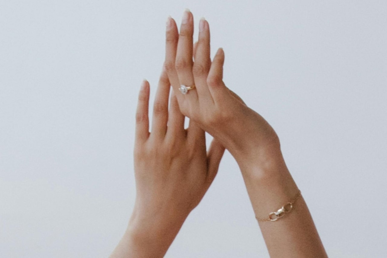 A close-up of a woman’s raised hands, an elegant halo ring on her finger and a delicate bracelet on her wrist.