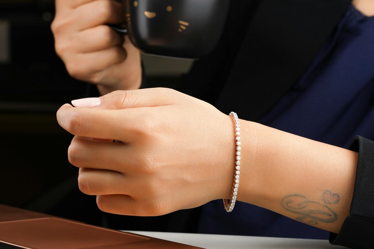 A close-up of a woman’s wrist, adorned with a delicate tennis bracelet, as she drinks from a coffee mug.