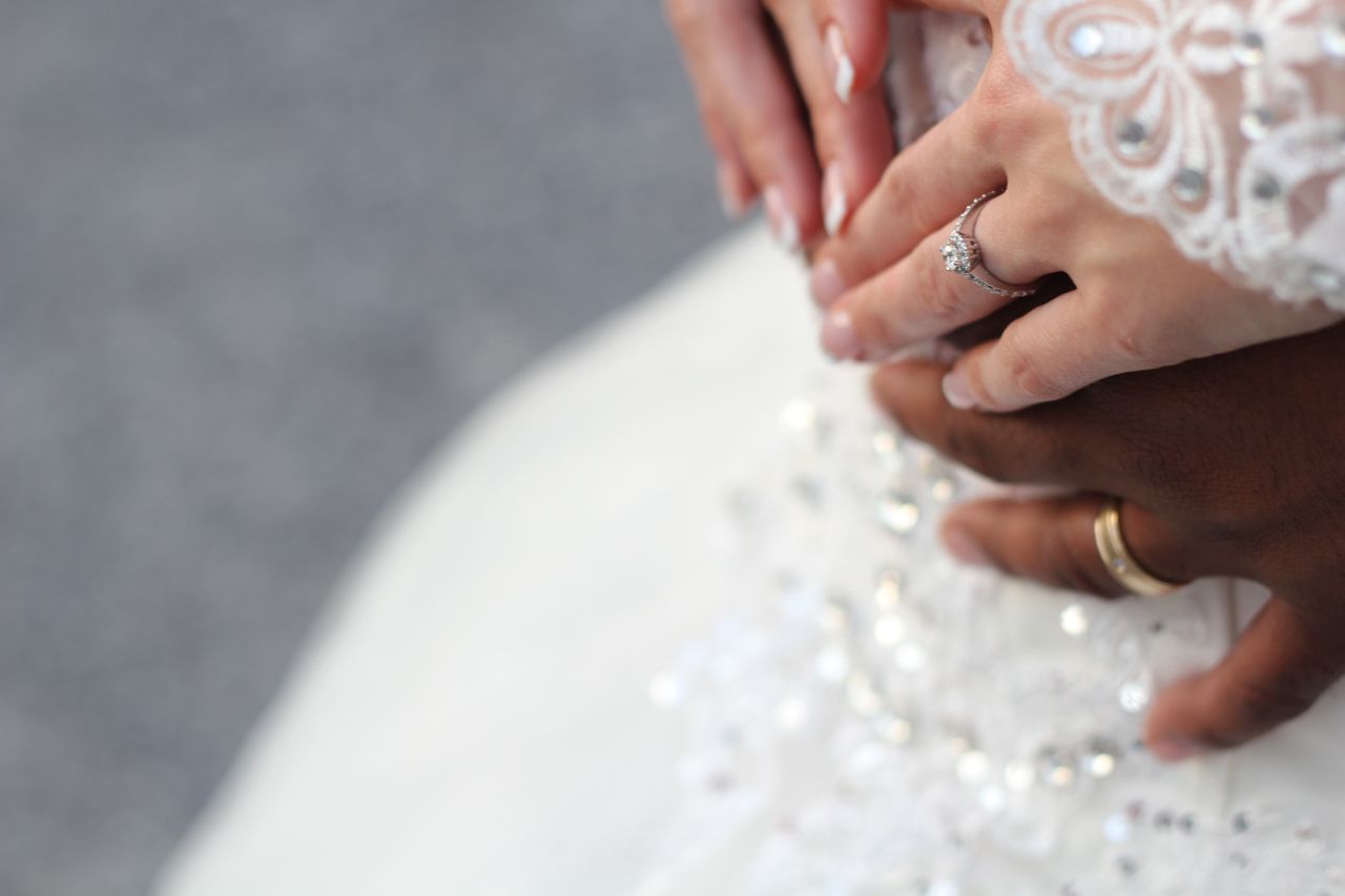 A close-up of a bride and groom’s hands placed over each other, showcasing their wedding rings against the bride’s shimmering gown. A close-up of a bride and groom’s hands placed over each other, showcasing their wedding rings against the bride’s shimmering gown.
