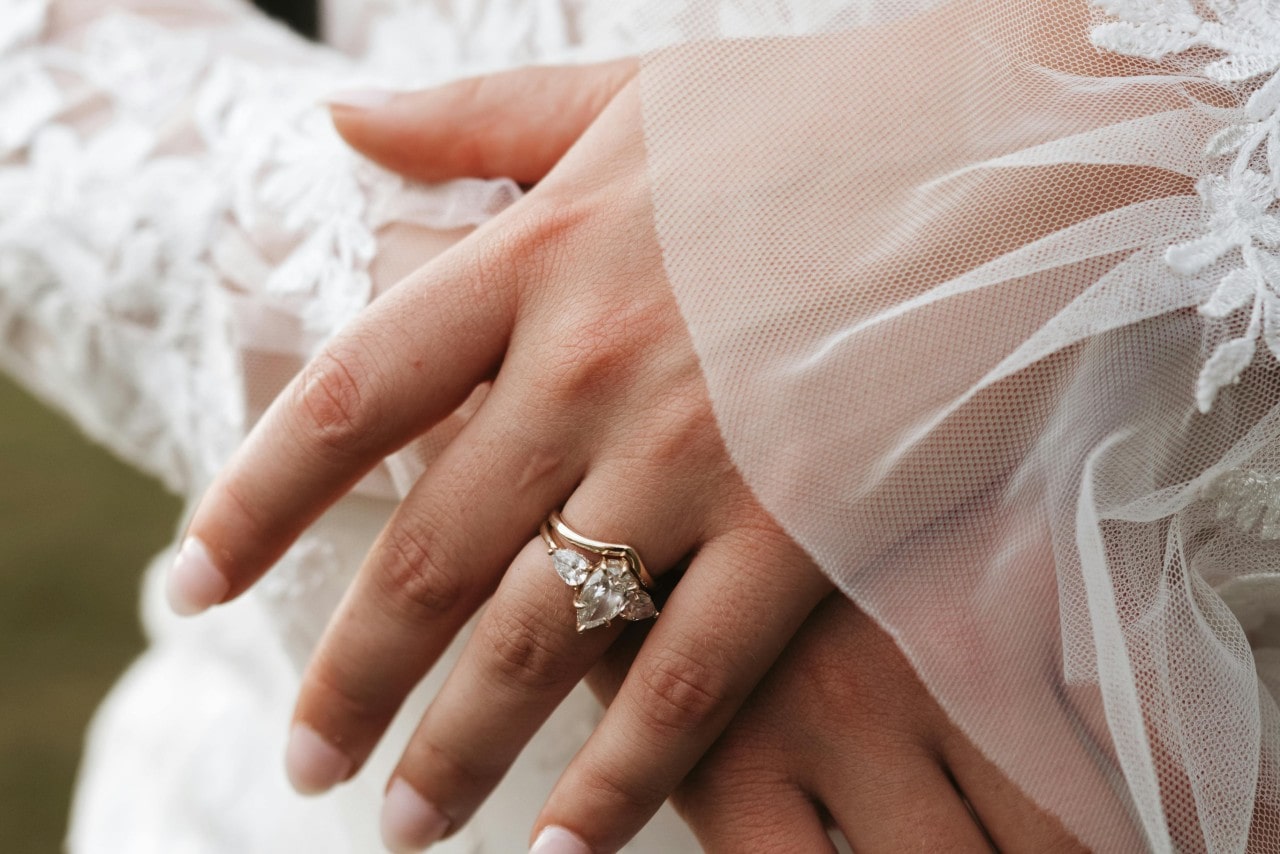 A close-up of a bride’s hands, with emphasis on her pear cut three stone engagement ring stacked with a simple wedding band.
