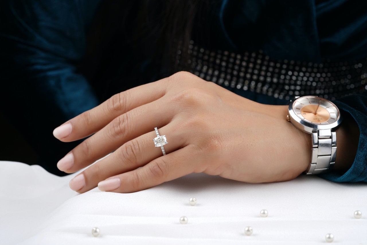 a woman’s hand resting on a white cushion wearing a radiant cut engagement ring