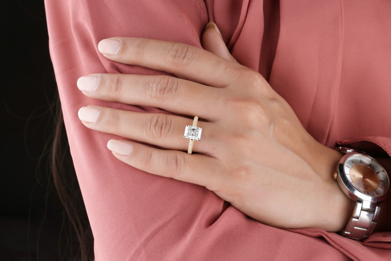 a woman’s hand resting on her arm wearing a radiant cut engagement ring