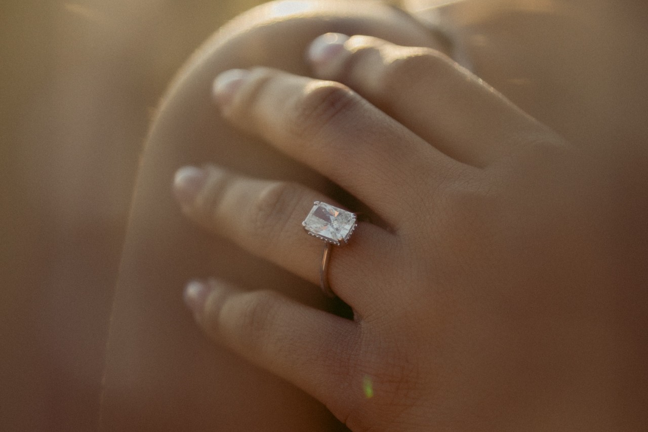 close up of a woman’s hand resting on her shoulder and wearing a solitaire engagement ring
