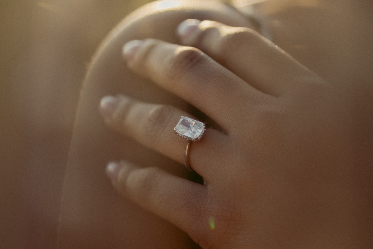 close up of a woman’s hand resting on her shoulder and wearing a solitaire engagement ring close up of a woman’s hand resting on her shoulder and wearing a solitaire engagement ring