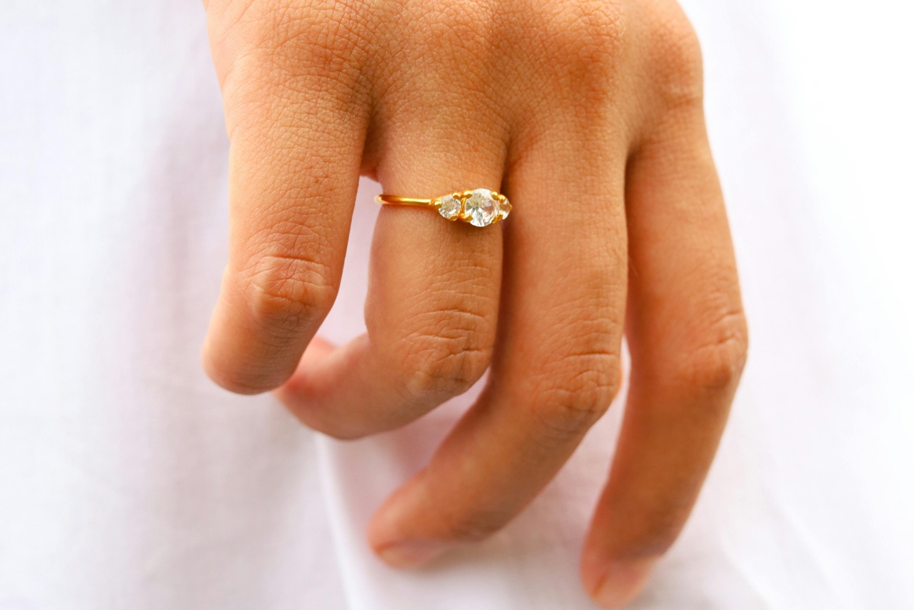 A close-up of a woman’s hand, adorned with a golden three-stone ring and a round center stone.