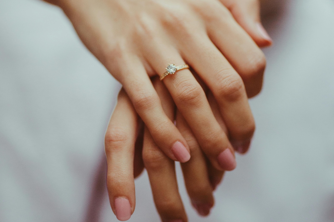 A woman’s hands laid on top of one another, showcasing her solitaire gold engagement ring with a round cut diamond.