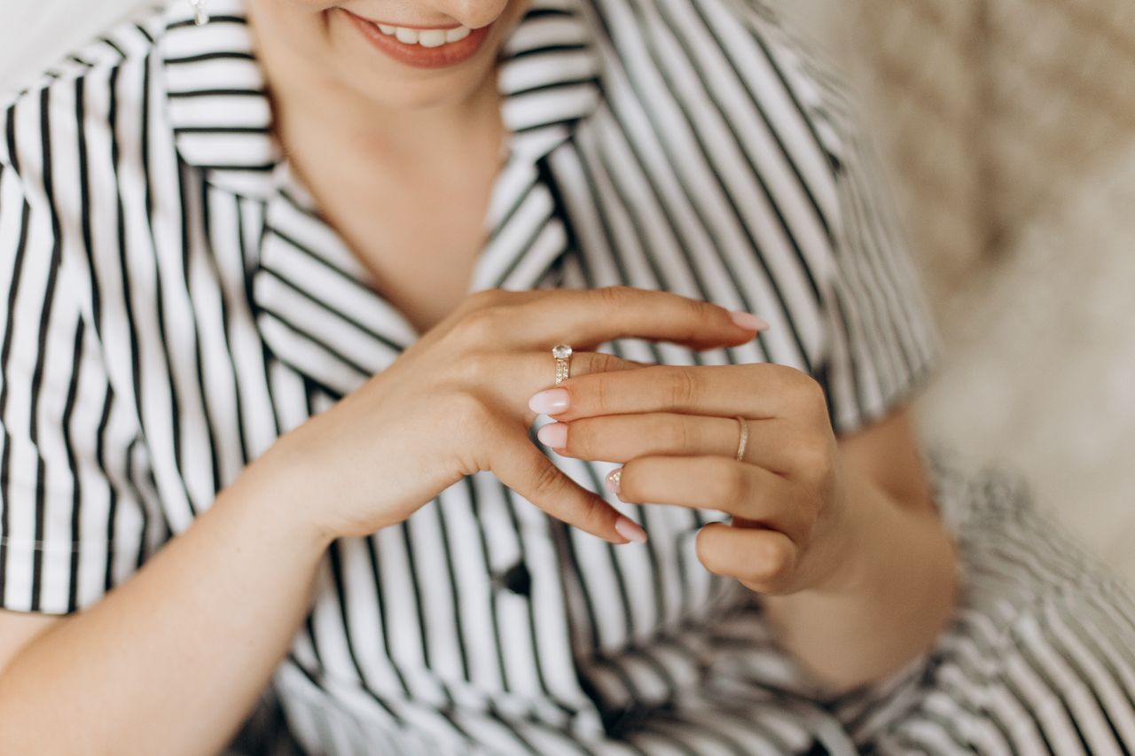 A woman slips a side stone engagement ring on her finger with a wedding band.