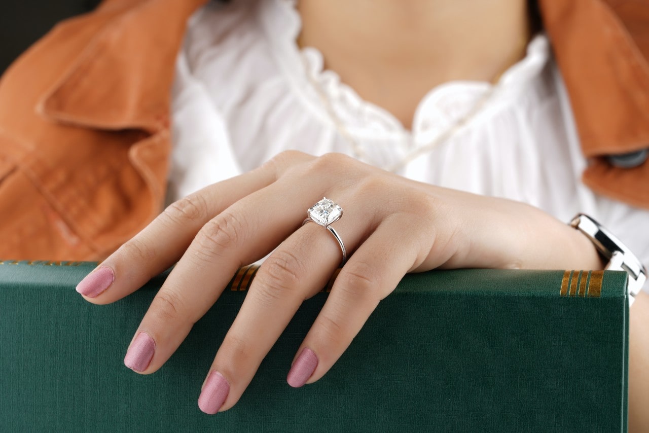 A woman’s hand resting on a book, wearing a solitaire engagement ring