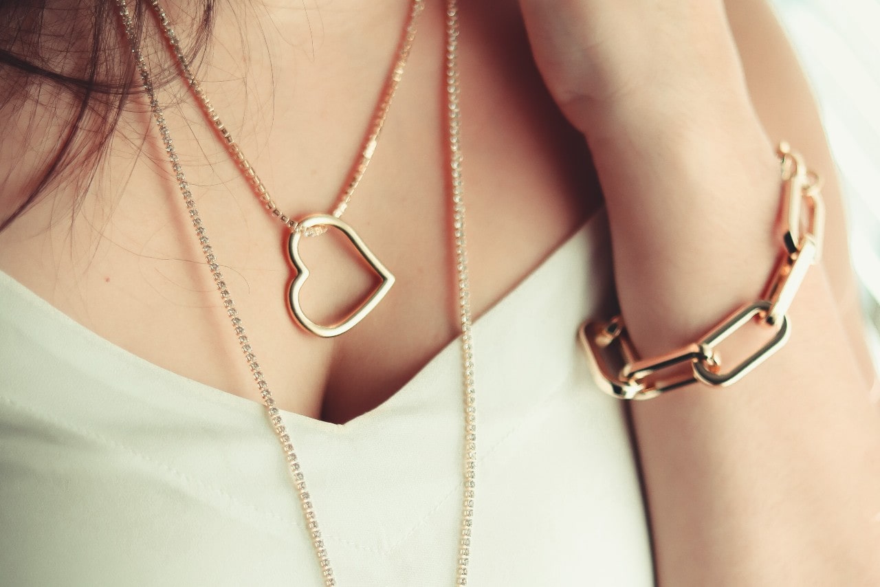 A woman wearing a gold heart-shaped pendant necklace and a chunky gold bracelet on her wrist.