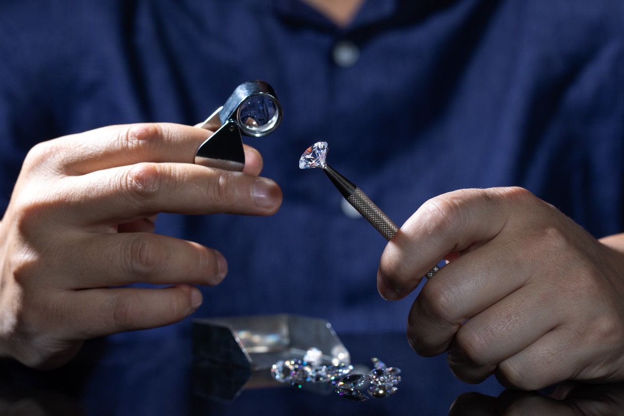 A jeweler in a dark blue shirt inspecting loose diamond with magnifying glass