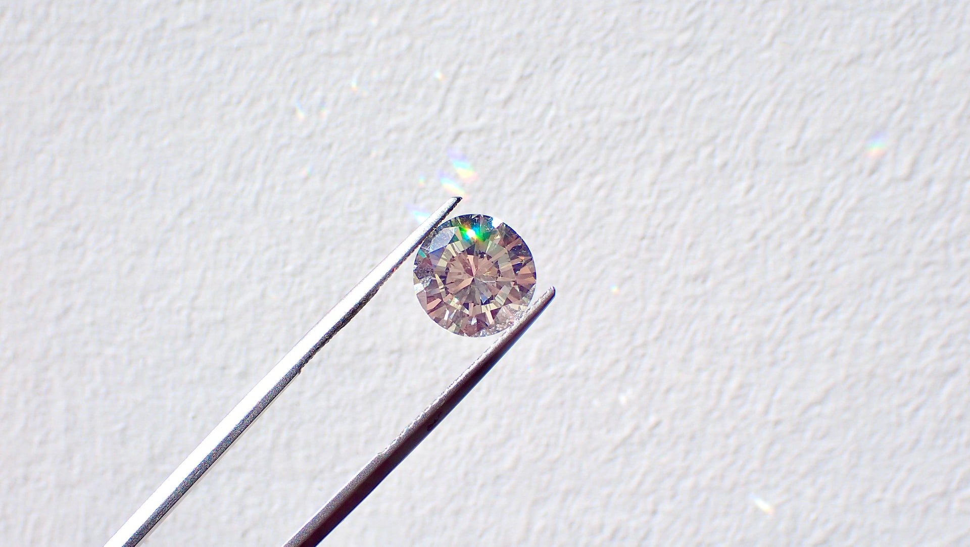 A round cut brilliant diamond held by tweezers against a white background