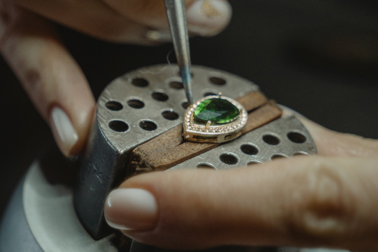 A close-up of a jeweler’s hands as they service a vibrant emerald pendant.