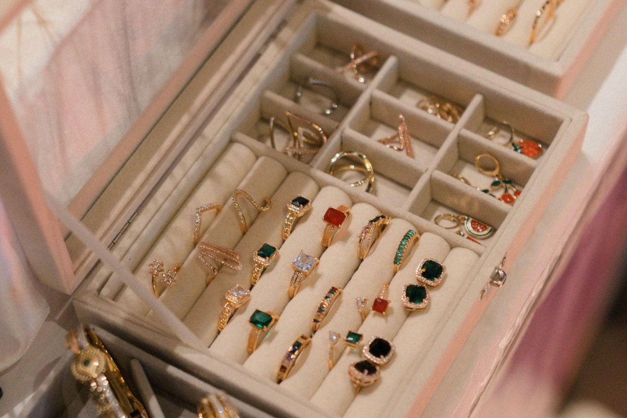 A top-down view of a large collection of gemstone rings, organized carefully in a plush glass-top jewelry box.